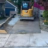 Yellow excavator parked on a driveway, with a concrete walkway and front yard on either side