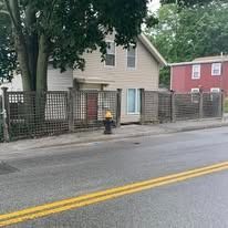 Residential street with beige house, fenced yard, and a fire hydrant by the road