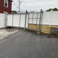 White fence and metal gate in a paved driveway beside a red building.