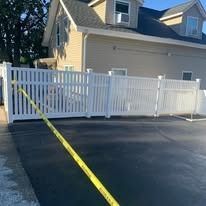 Yellow caution tape across a paved driveway in front of a white fence and beige house.