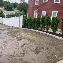 Curved driveway beside a red house, with white fence and lined shrubs along the edge