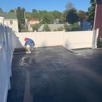 Worker spreading black rooftop coating on a flat roof under a clear blue sky
