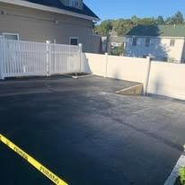 Empty blacktop driveway with a white fence and low wall beside a house.