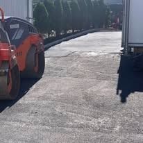 Construction vehicles on a sunlit paved road, including an orange roller and a white truck