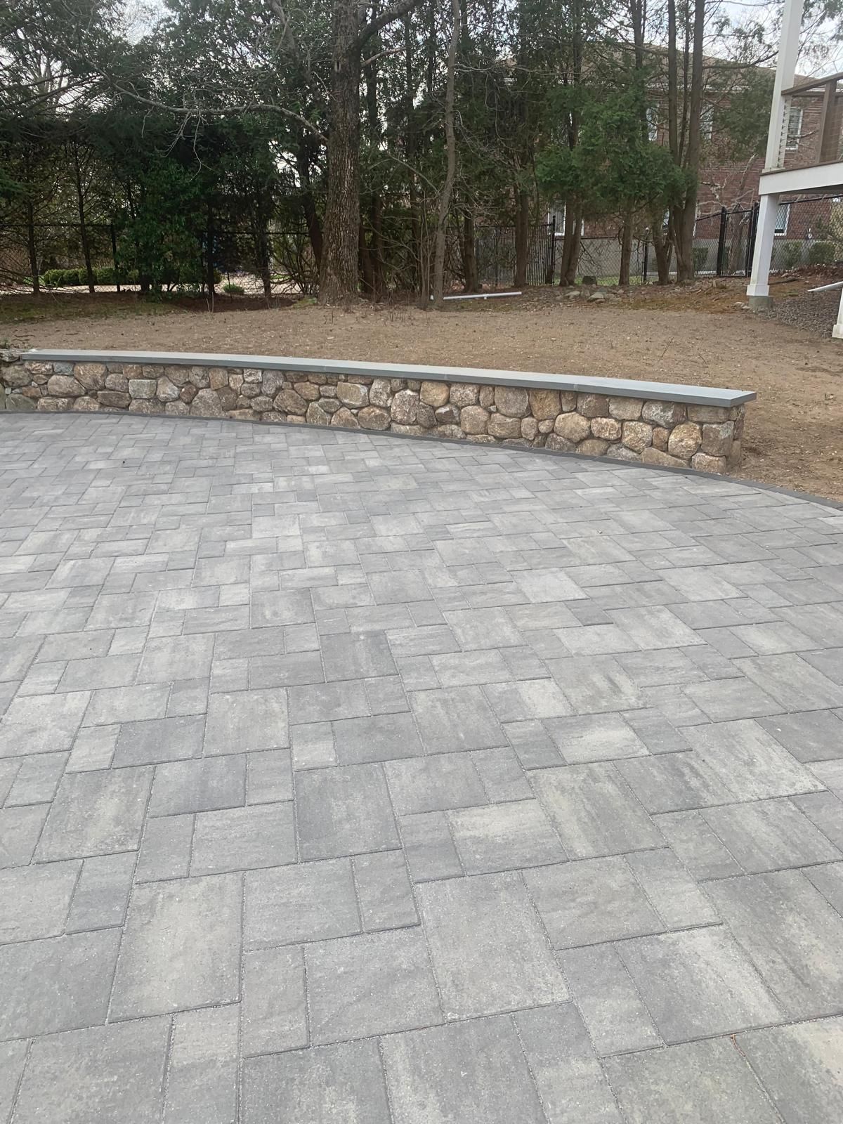 Paved stone courtyard with a low stone wall and trees in the background.