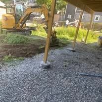 Gravel patio under a wooden deck, with support posts and an excavator in the background.