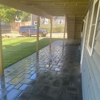 Covered porch with glossy black tile floor, blue house siding, and a lawn view outside