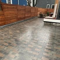 Empty backyard patio with wet brick pavers and a wood fence along the left side