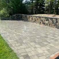 Paved stone patio with a low stone wall beside a grassy yard and trees