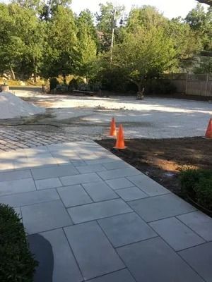 Paved walkway beside a gravel area with orange cones and trees in the background