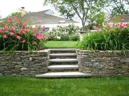 Stone steps lead up through a flower garden to a house, with pink blooms and green lawn.