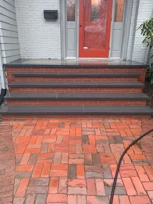 Front stoop with red door, dark steps, and a brick-paved walkway.