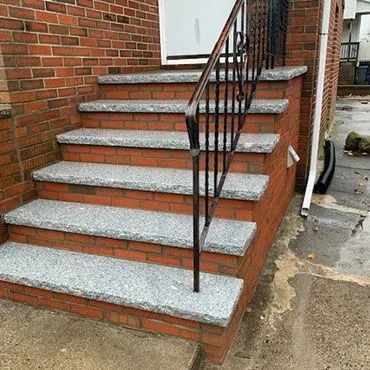 Brick front steps with gray stone treads and a black metal handrail beside a house entrance