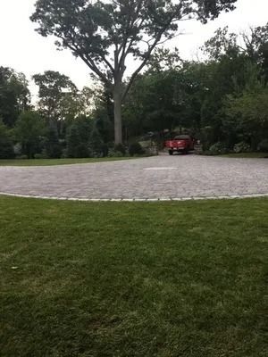 Red vehicle parked on a circular stone drive in a wooded park with grass in the foreground.