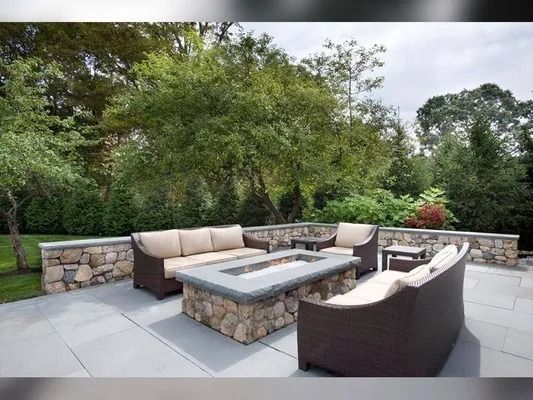 Outdoor patio with stone fire pit, wicker seating, and lush garden backdrop