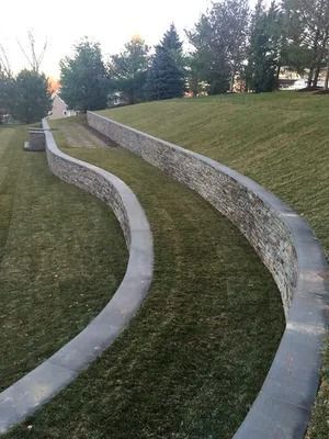 Curving concrete retaining walls on a grassy hillside with trees in the background