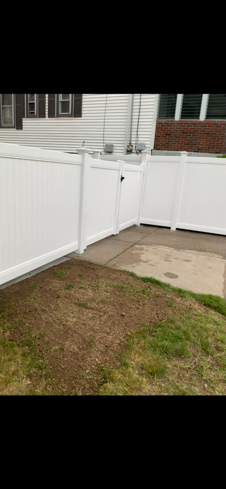 White vinyl fence corner beside a house with a patch of grass and concrete walkway.