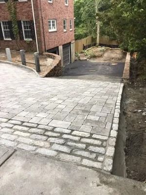 Cobblestone driveway ramp beside a brick building, leading down to a lower paved area.