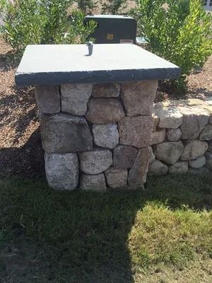 Stone outdoor barbecue grill with a light countertop and black cover in a sunny yard