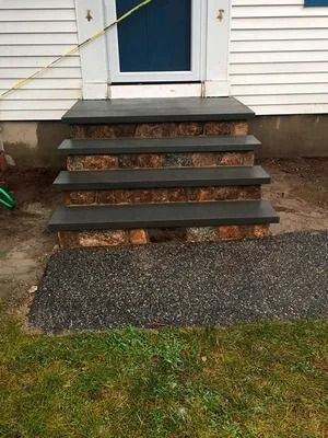 Front steps to a white house with a dark blue door and a short gravel path.