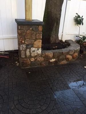 Stone planter around a tree beside a white wall on a wet patterned patio