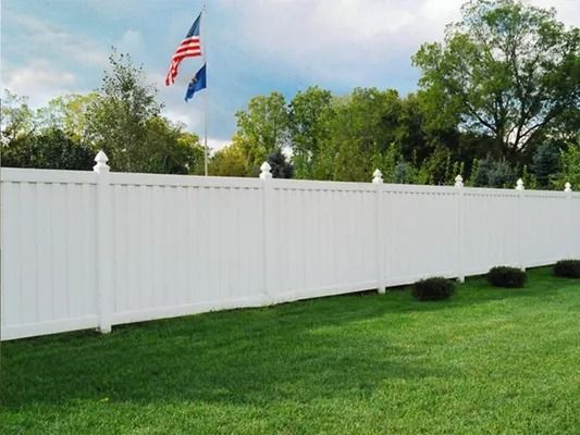 White vinyl fence along a green lawn with an American flag flying above it.