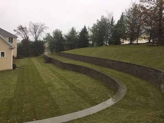 Curved concrete path beside a grassy terraced hillside near houses and trees