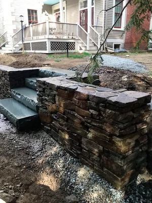 Stone retaining wall with steps in a muddy backyard patio area near a house porch