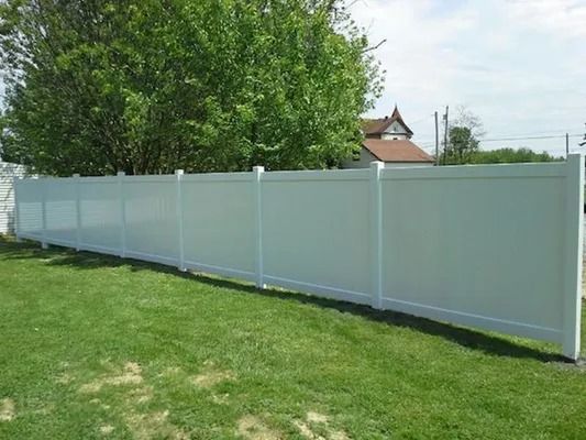 White fence along a grassy yard beside a large green tree on a sunny day