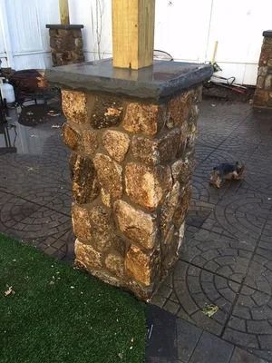 Stone pillar with a wooden post on a wet patterned patio, with small dogs in the background.