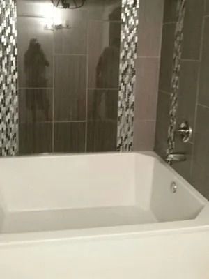 Modern bathroom with a white bathtub and tiled shower wall with mosaic accents