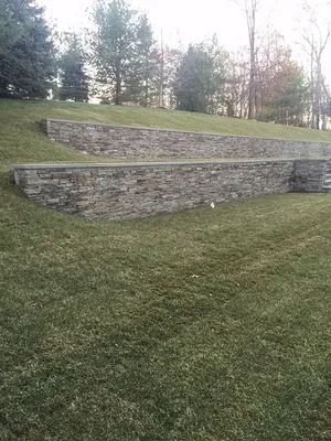 Terraced stone retaining walls on a grassy hillside with trees in the background