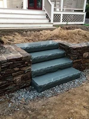 Stone front steps with blue-gray treads leading to a house porch, surrounded by dirt and gravel