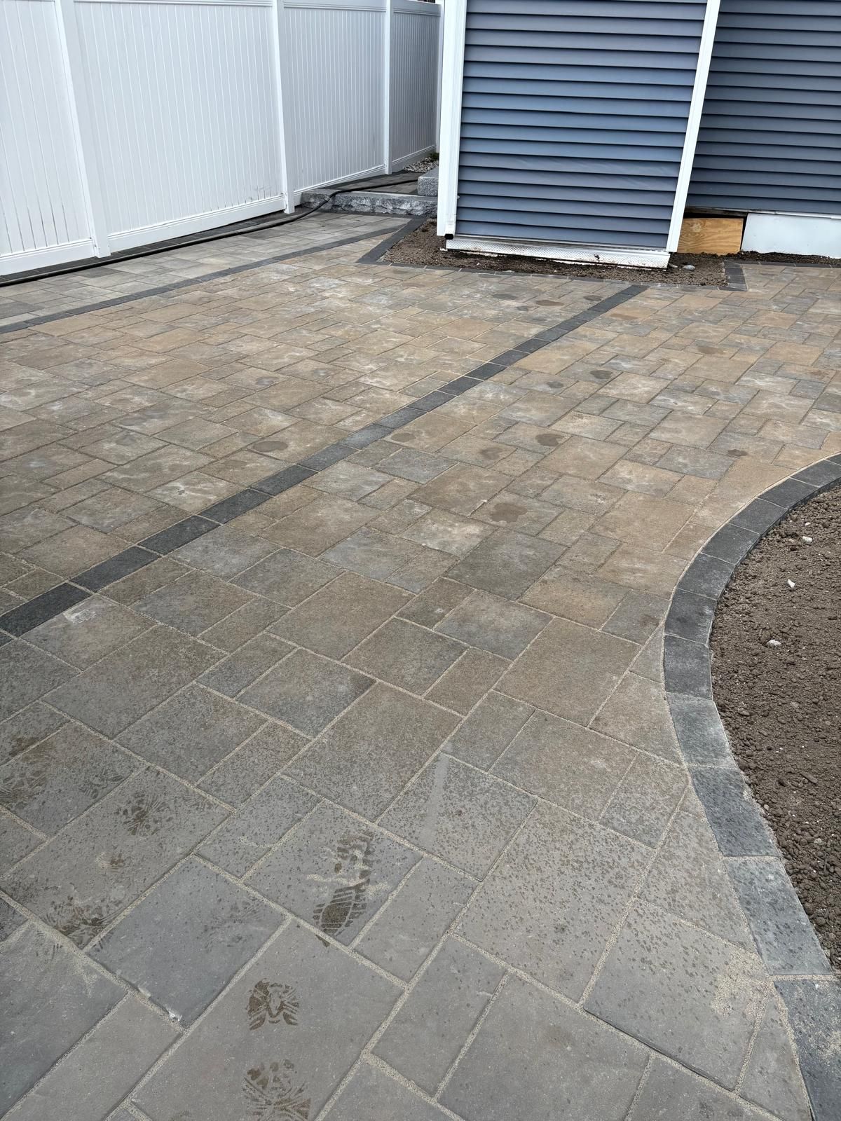 Stone patio beside a shed and white fence, with a curved gravel edge.