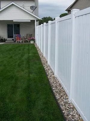 Backyard with green lawn beside a white vinyl fence and gray house porch