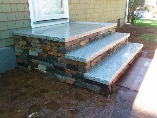Stone front steps with concrete treads beside a house porch, viewed from the yard.
