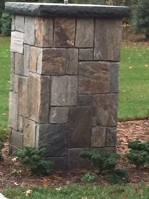 Stone utility pillar with a flat cap, set in a mulched lawn by grass and shrubs.