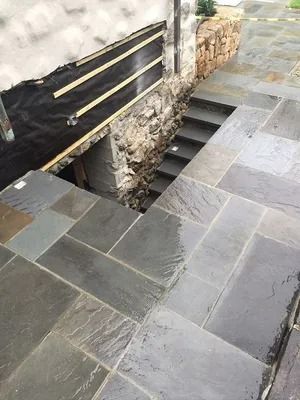 Stone steps beside a black railing and rough stone wall, leading down into a narrow passage.