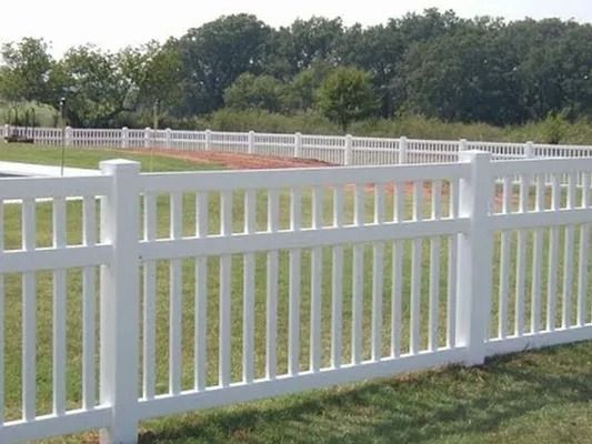 White vinyl fence beside a grassy field with trees in the background