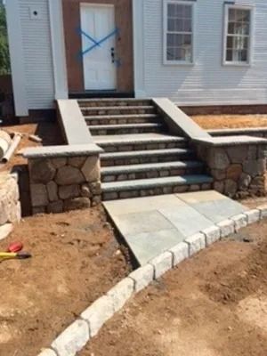 Front steps leading to a house entrance, with stone retaining walls and a curved concrete walkway.