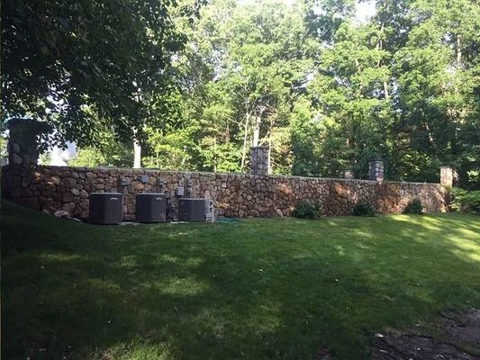 Stone wall with trash bins beside a grassy lawn and trees in a sunny park