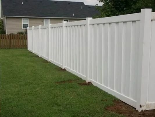 White vinyl fence along a green lawn beside a house in a suburban yard