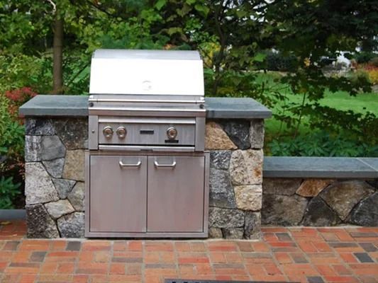Outdoor stainless steel grill built into a stone-and-brick patio counter in a backyard