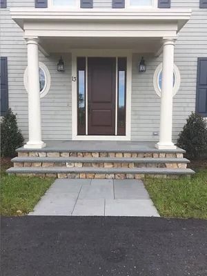 Front entrance of a house with white columns, dark door, and stone steps leading up from a walkway