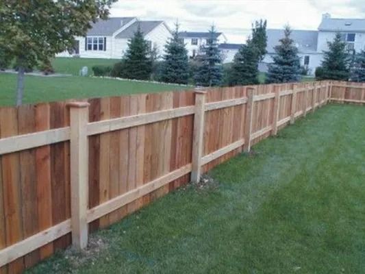 Wooden privacy fence along a grassy yard with houses and trees in the background