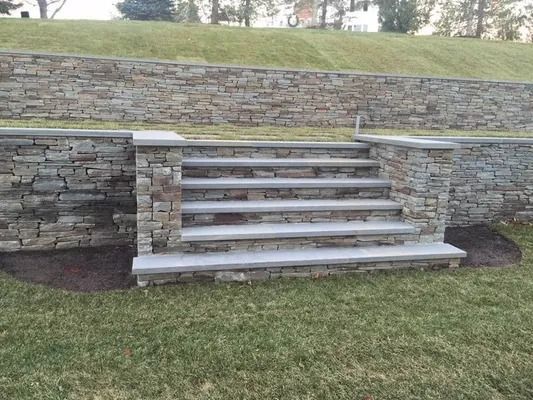 Stone steps built into a retaining wall on a grassy slope.