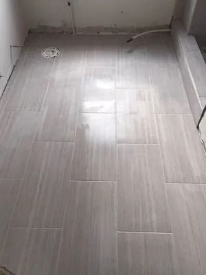 Empty tiled bathroom floor with a drain and exposed pipe near the wall