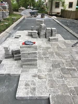 Paver stones being laid on a driveway, with stacks of gray bricks and a trowel in the foreground