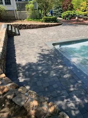 Stone pool deck with a swimming pool, built-in bench, and landscaped garden in sunlight
