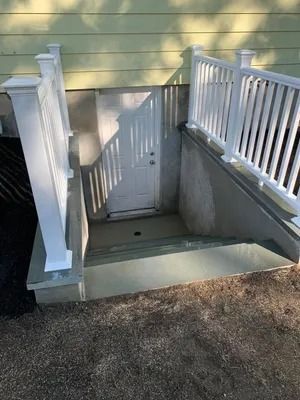 Front steps with white railings leading down to a basement door on a yellow house